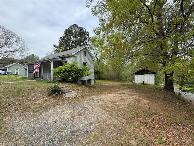 view of side of property featuring an outdoor structure, a sunroom, a shed, and dirt driveway