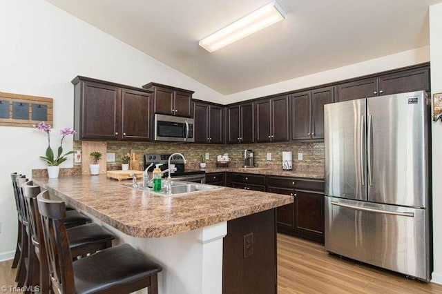 kitchen with appliances with stainless steel finishes, vaulted ceiling, dark brown cabinetry, a sink, and a peninsula