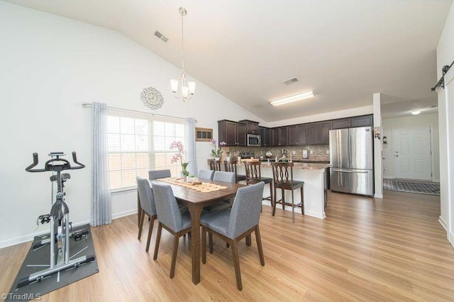 dining area featuring vaulted ceiling, a chandelier, light wood finished floors, a barn door, and baseboards