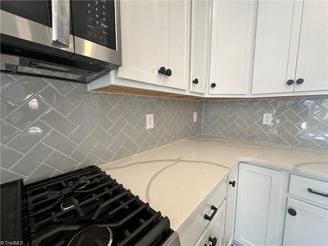 kitchen with backsplash, stainless steel microwave, white cabinetry, and light stone countertops