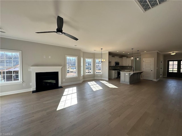 unfurnished living room with a sink, baseboards, a ceiling fan, and dark wood finished floors