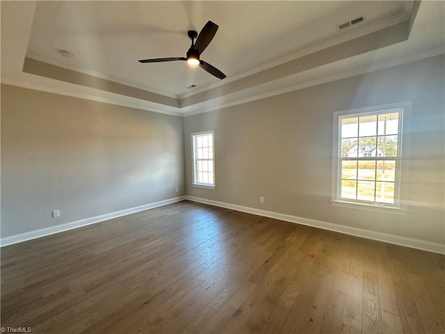 empty room with ornamental molding, a tray ceiling, and dark wood finished floors