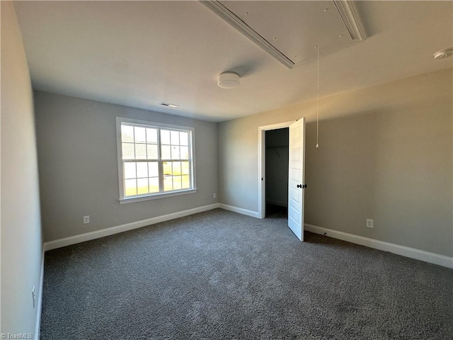 empty room featuring dark carpet, attic access, baseboards, and visible vents