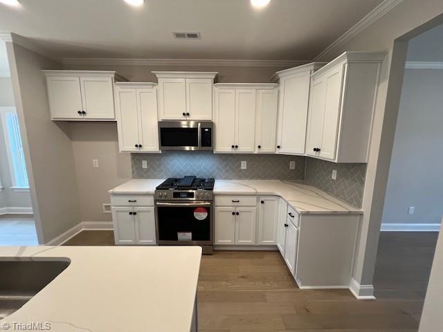 kitchen featuring white cabinetry, ornamental molding, appliances with stainless steel finishes, hardwood / wood-style flooring, and backsplash