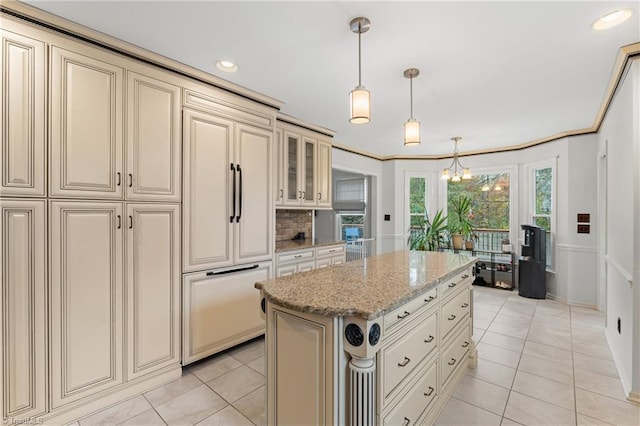 kitchen featuring cream cabinets, paneled fridge, light stone countertops, pendant lighting, and a center island