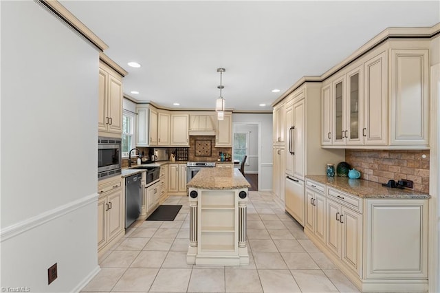 kitchen with a center island, built in appliances, hanging light fixtures, light stone countertops, and cream cabinetry