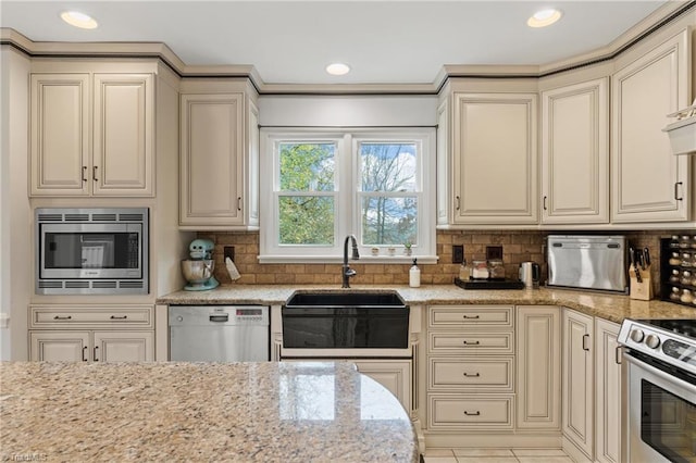 kitchen with decorative backsplash, stainless steel appliances, sink, and cream cabinetry