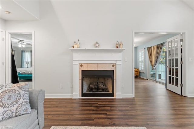 living room with dark wood-type flooring, a tiled fireplace, lofted ceiling, and ceiling fan