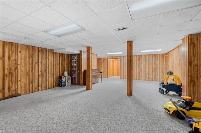 basement with wooden walls, carpet flooring, and a paneled ceiling