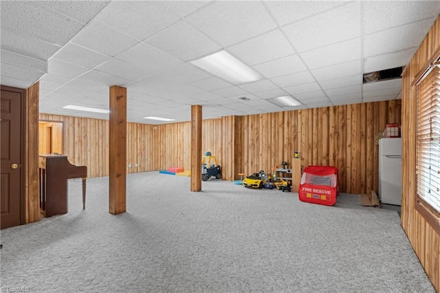 rec room with wood walls, a drop ceiling, and carpet