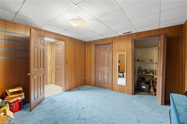 bedroom featuring wooden walls, a drop ceiling, and light carpet