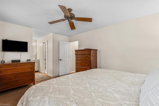 bedroom with a textured ceiling, ensuite bath, baseboards, and ceiling fan