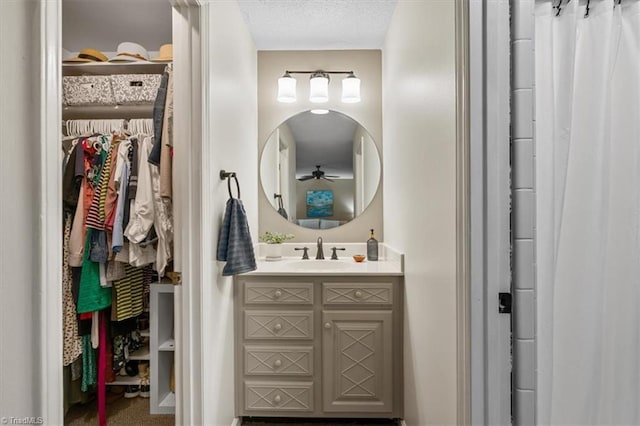 full bathroom with vanity, a textured ceiling, a walk in closet, and a ceiling fan