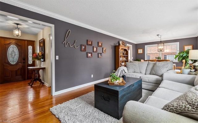 living room featuring wood finished floors, baseboards, a textured ceiling, crown molding, and a chandelier