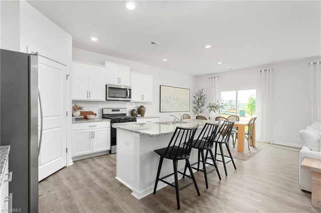 kitchen with light stone countertops, stainless steel appliances, a breakfast bar area, a center island with sink, and white cabinets