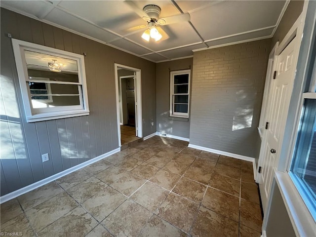 empty room featuring ceiling fan and wooden walls