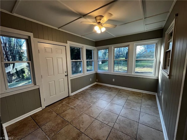 tiled entryway with ceiling fan, wooden walls, and crown molding