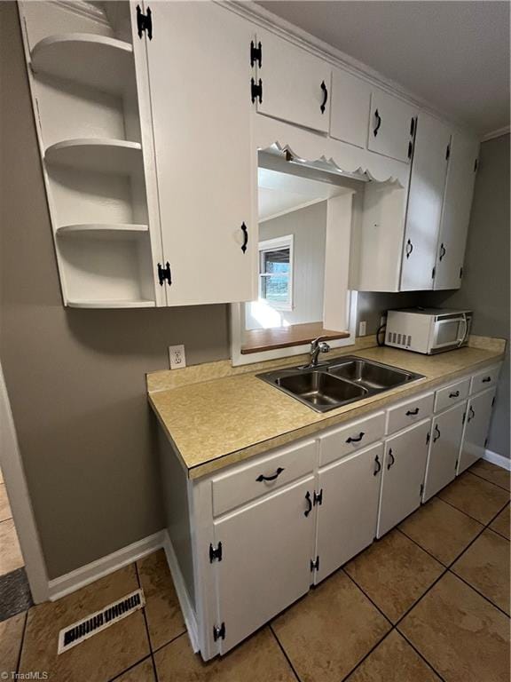 kitchen with white cabinetry, sink, light tile patterned flooring, and ornamental molding