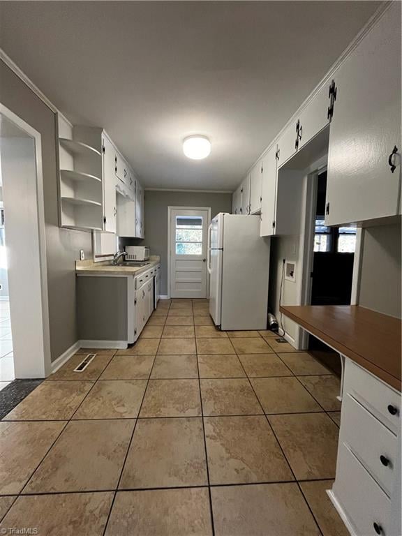 kitchen with white refrigerator, white cabinetry, ornamental molding, and light tile patterned flooring