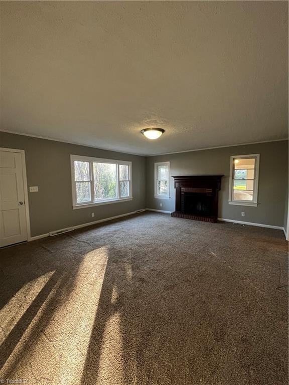 unfurnished living room featuring a wealth of natural light, dark colored carpet, a textured ceiling, and a brick fireplace