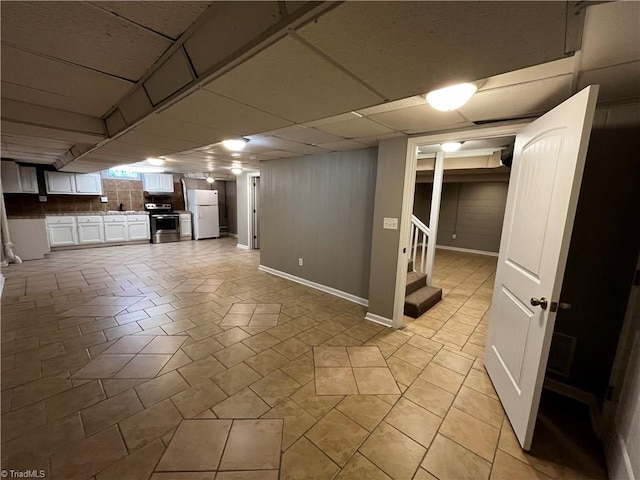 basement featuring light tile patterned floors, white refrigerator, and a drop ceiling