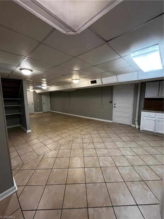 basement with a drop ceiling and light tile patterned floors