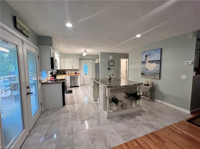 kitchen with a center island, a textured ceiling, stainless steel appliances, baseboards, and white cabinetry