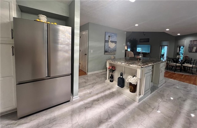 kitchen featuring recessed lighting, freestanding refrigerator, light stone countertops, a kitchen island, and baseboards