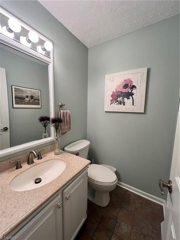 bathroom with a textured ceiling, toilet, baseboards, tile patterned flooring, and vanity