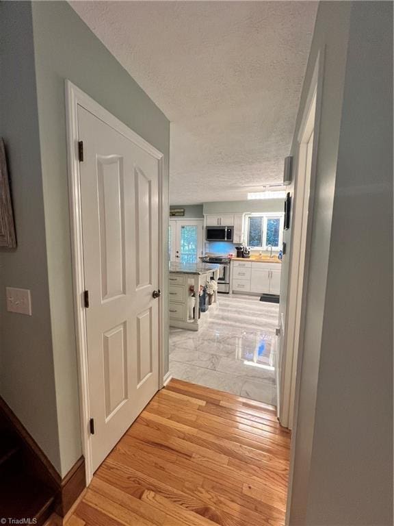 hall featuring a sink, a textured ceiling, and light wood-style floors