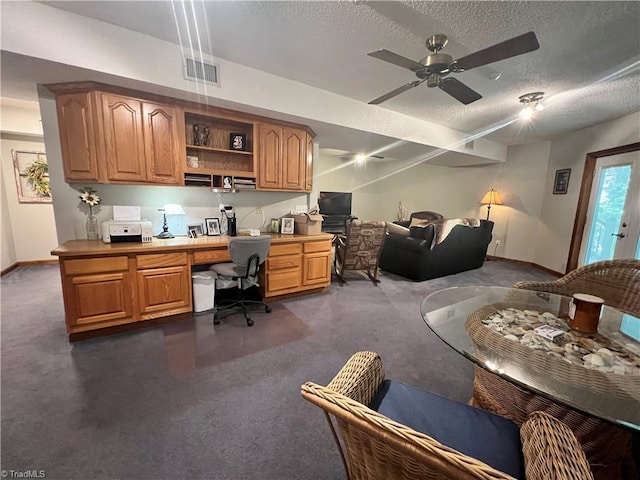 office area with built in desk, dark carpet, visible vents, baseboards, and ceiling fan