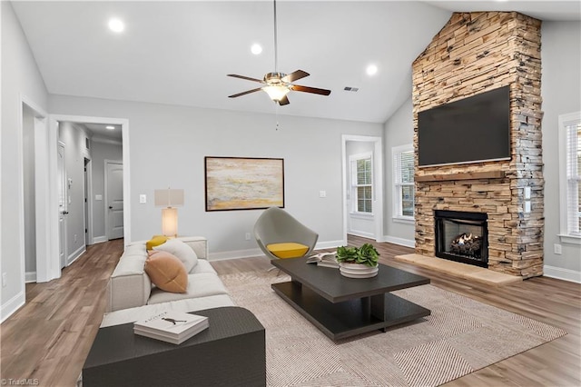 living room featuring high vaulted ceiling, light hardwood / wood-style floors, a stone fireplace, and ceiling fan