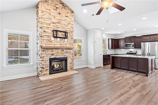 kitchen featuring vaulted ceiling, light hardwood / wood-style floors, a stone fireplace, stainless steel appliances, and dark brown cabinets