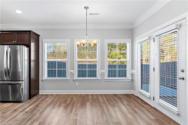 unfurnished dining area featuring light hardwood / wood-style floors, crown molding, and a chandelier