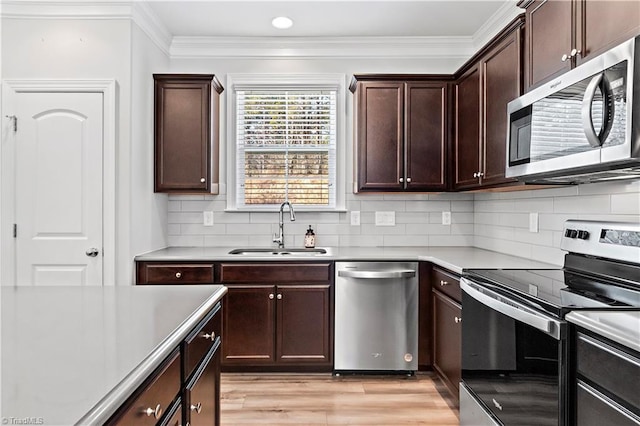 kitchen with appliances with stainless steel finishes, backsplash, crown molding, light hardwood / wood-style flooring, and sink