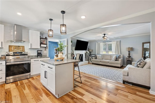5215 Hicone Rd, Mcleansville, NC 27301 - kitchen featuring electric stove, wall chimney exhaust hood, a ceiling fan, white cabinetry, and a kitchen breakfast bar