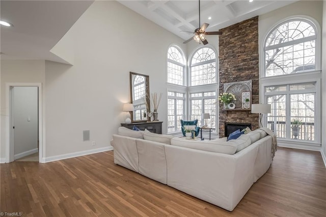 living room with a high ceiling, coffered ceiling, hardwood / wood-style floors, and a stone fireplace