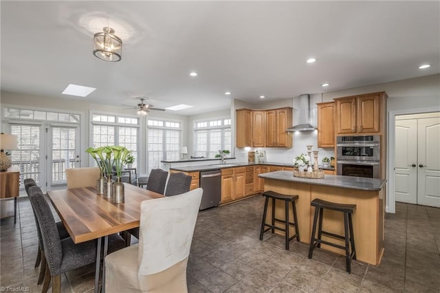 kitchen featuring sink, wall chimney exhaust hood, stainless steel appliances, a skylight, and ceiling fan