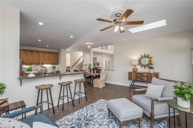 tiled living room with ceiling fan and a skylight