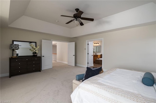 carpeted bedroom with ceiling fan, a tray ceiling, and ensuite bath