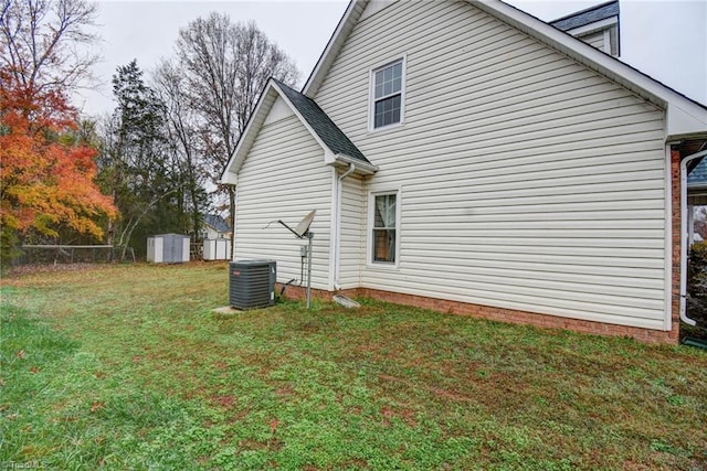 view of side of home with a yard, cooling unit, and a storage shed