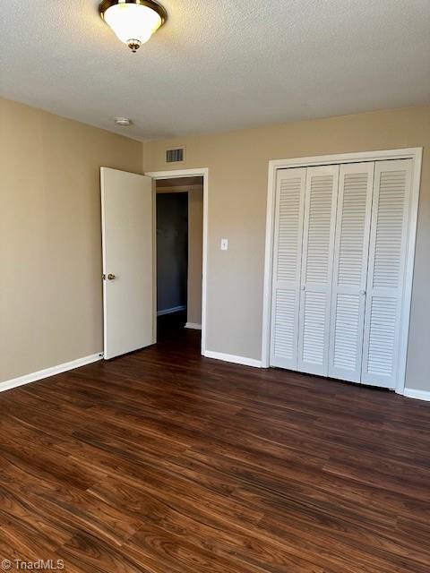 unfurnished bedroom with dark hardwood / wood-style flooring, a closet, and a textured ceiling