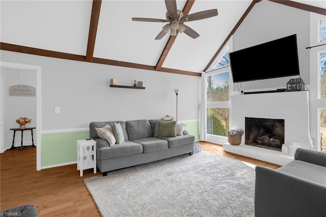 living area with beam ceiling, a ceiling fan, a brick fireplace, wood finished floors, and high vaulted ceiling