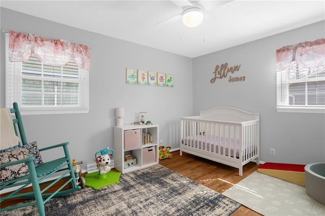 bedroom with a nursery area, ceiling fan, baseboards, and wood finished floors