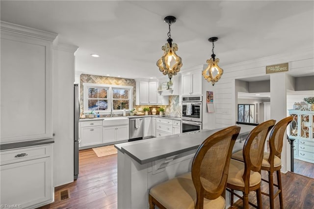 kitchen with pendant lighting, dark hardwood / wood-style floors, appliances with stainless steel finishes, a kitchen bar, and white cabinetry