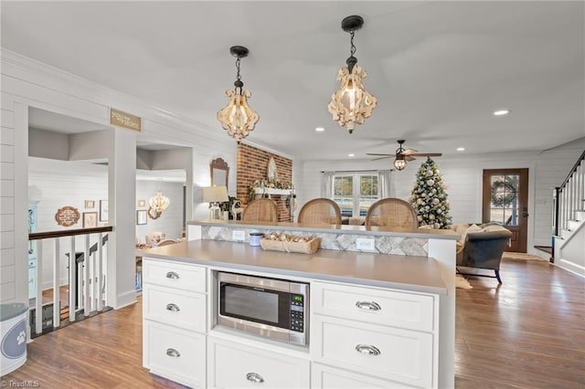 kitchen featuring ceiling fan, hanging light fixtures, wood-type flooring, white cabinets, and stainless steel microwave