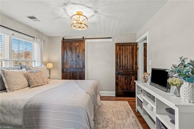 bedroom featuring dark hardwood / wood-style flooring, a barn door, and a notable chandelier