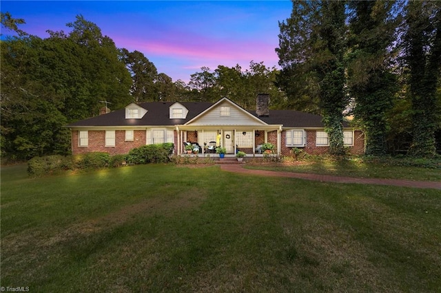 view of front of house featuring a chimney, a porch, brick siding, and a front yard