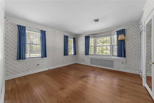 unfurnished bedroom featuring visible vents, baseboards, multiple windows, and hardwood / wood-style flooring
