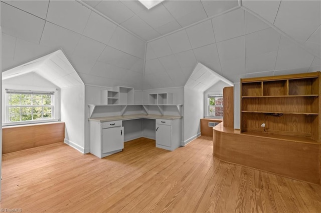 unfurnished office featuring a healthy amount of sunlight, vaulted ceiling, built in study area, and light wood-style flooring